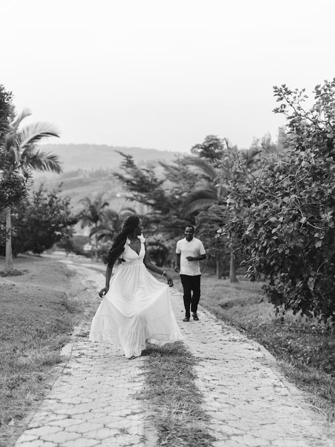 Celine twirling her white dress on a garden path as Khalim walks towards her